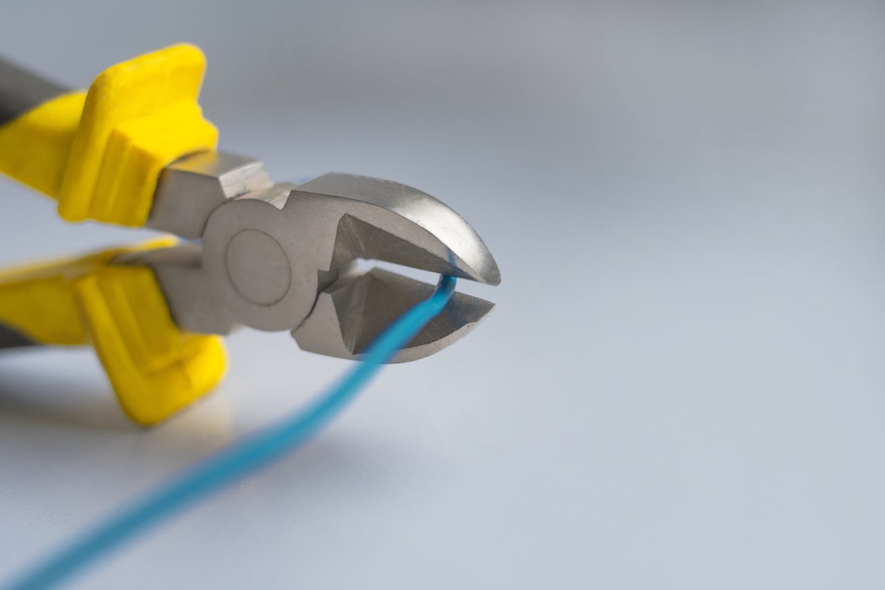 Macro shot of metal pliers with yellow handles cutting a blue wire against a gray background.