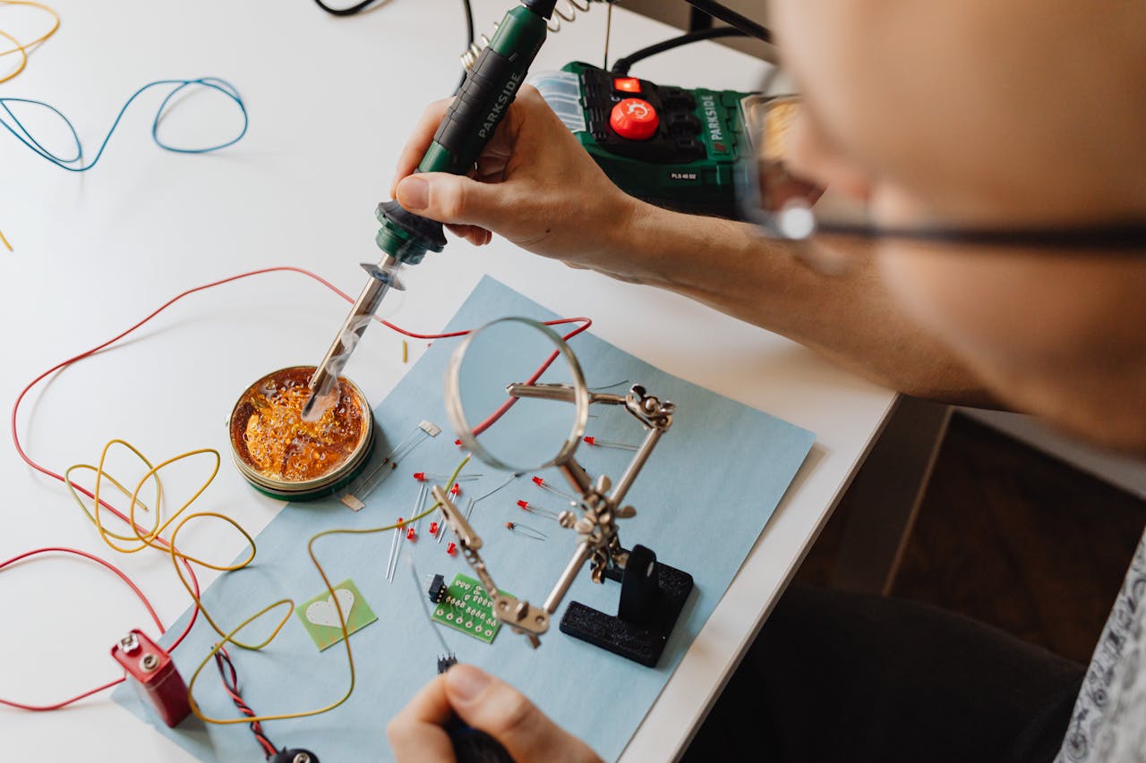 A technician skillfully soldering electronics with precision tools and wires on a workbench.